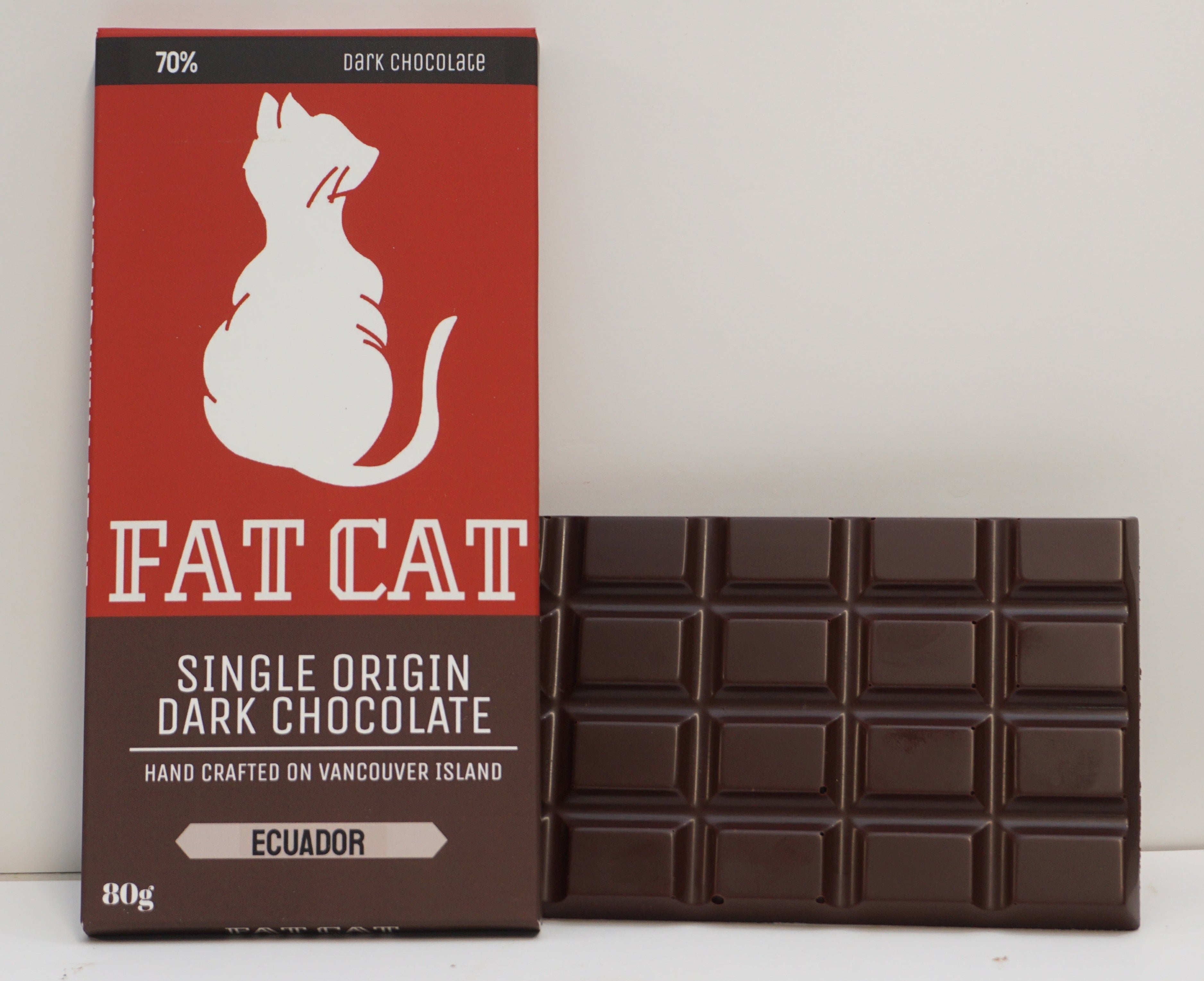 A bar of dark chocolate next to its red and brown packaging box, featuring a white cat silhouette and the brand name 'FAT CAT'.